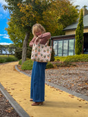 Person holding a floral tote bag outdoors with trees and a building in the background